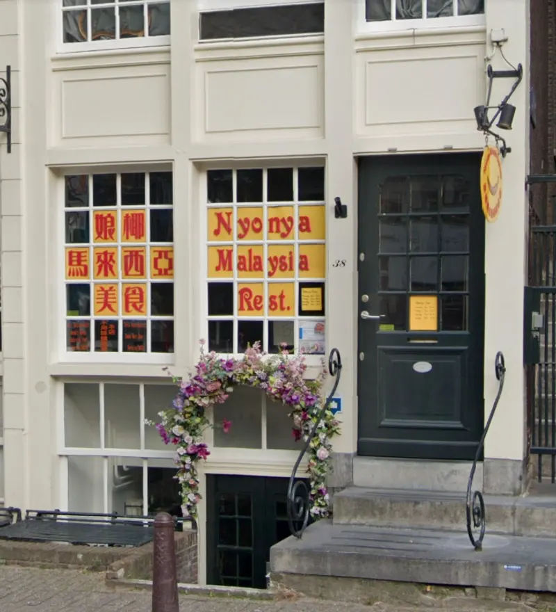 The Nyonya storefront on Kloveniersburgwal with yellow window letters and a flower arch